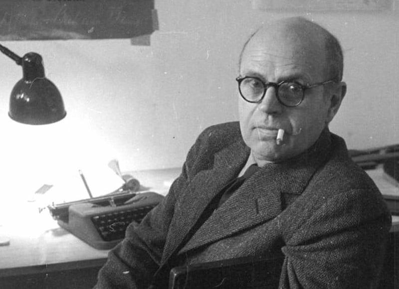 Arkitekt Poul Henningsen, ca. 1950. Portræt ved skrivebord iført jakke og med briller og tændt cigaret.